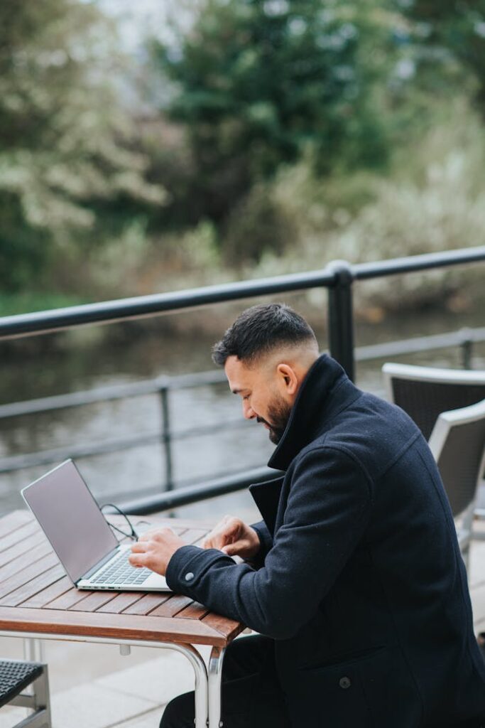 Attentive ethnic businessman working on laptop on cafe terrace